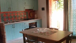 A kitchen with teal cabinets, a tiled backsplash, and a dining table with chairs. - Head of four terraced houses (Porto Corallo)