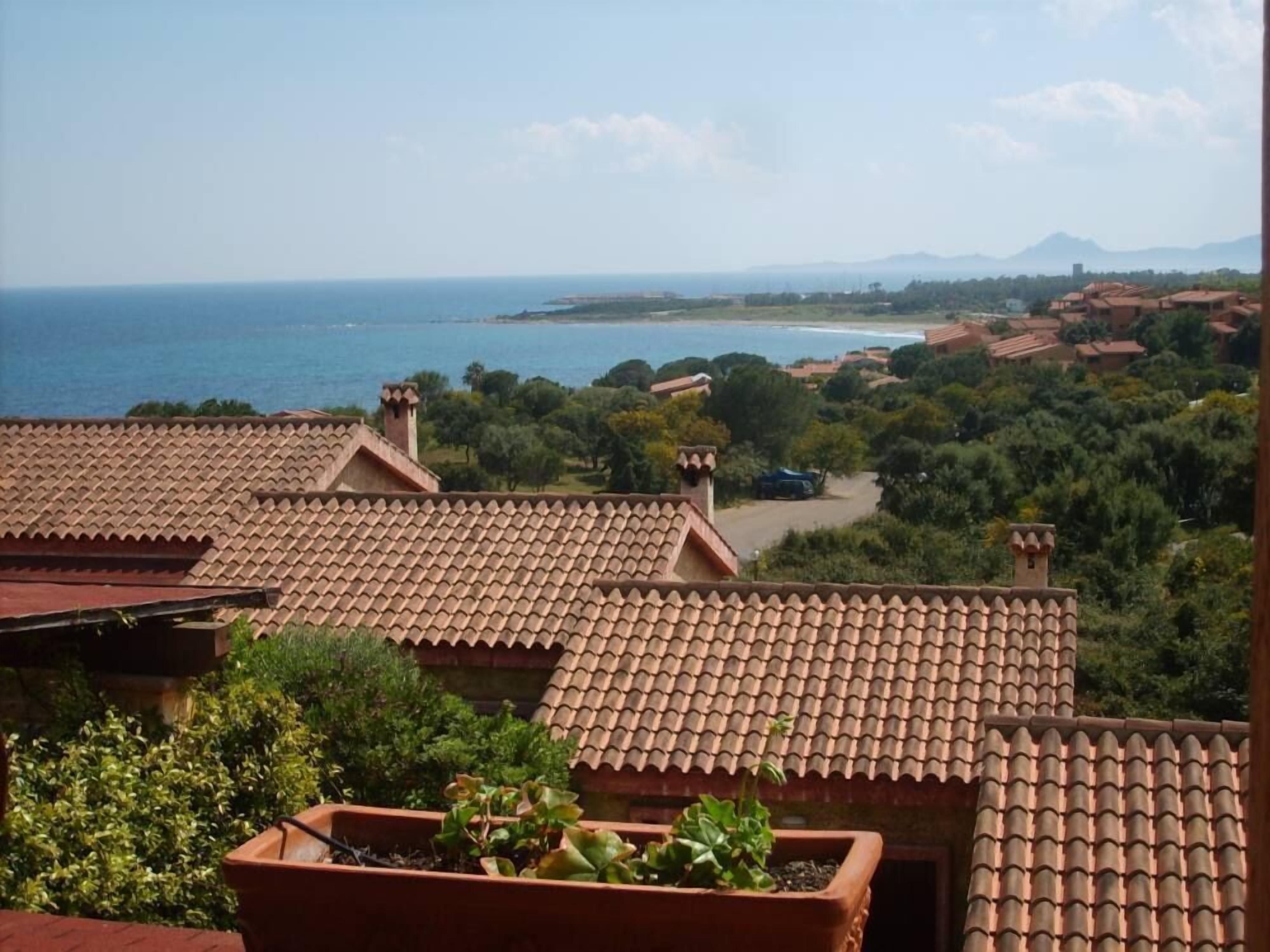 A coastal view with terracotta-tiled rooftops and lush greenery.
