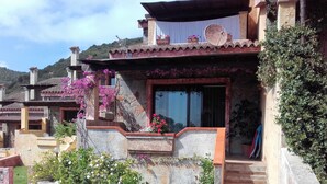 A traditional Mediterranean-style house with a stone facade, a balcony with potted plants, and a visible satellite dish. - Head of four terraced houses (Porto Corallo)
