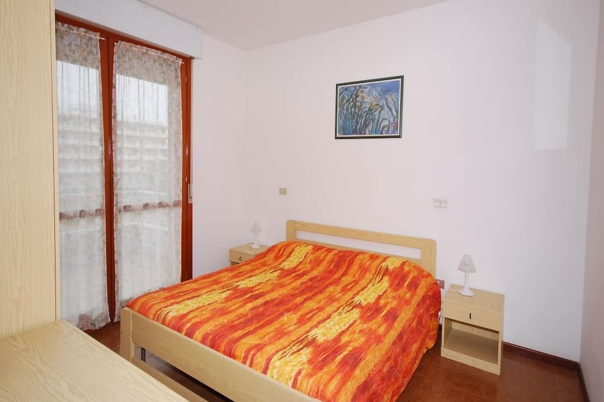 Une chambre à coucher comprenant un lit, deux tables de chevet, une commode, une armoire en bois et une fenêtre avec des rideaux.