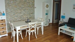 A dining area with a white table and chairs, a clock, and a cabinet with glass doors. - Residence Gardenia (Lignano Sabbiadoro)