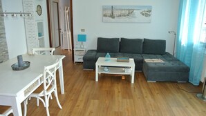 A living room with a white table, grey sofa, and a painting on the wall. - Residence Gardenia (Lignano Sabbiadoro)