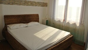 A room with a large bed, a nightstand, a lamp, and a window with sheer curtains. - Residence Gardenia (Lignano Sabbiadoro)