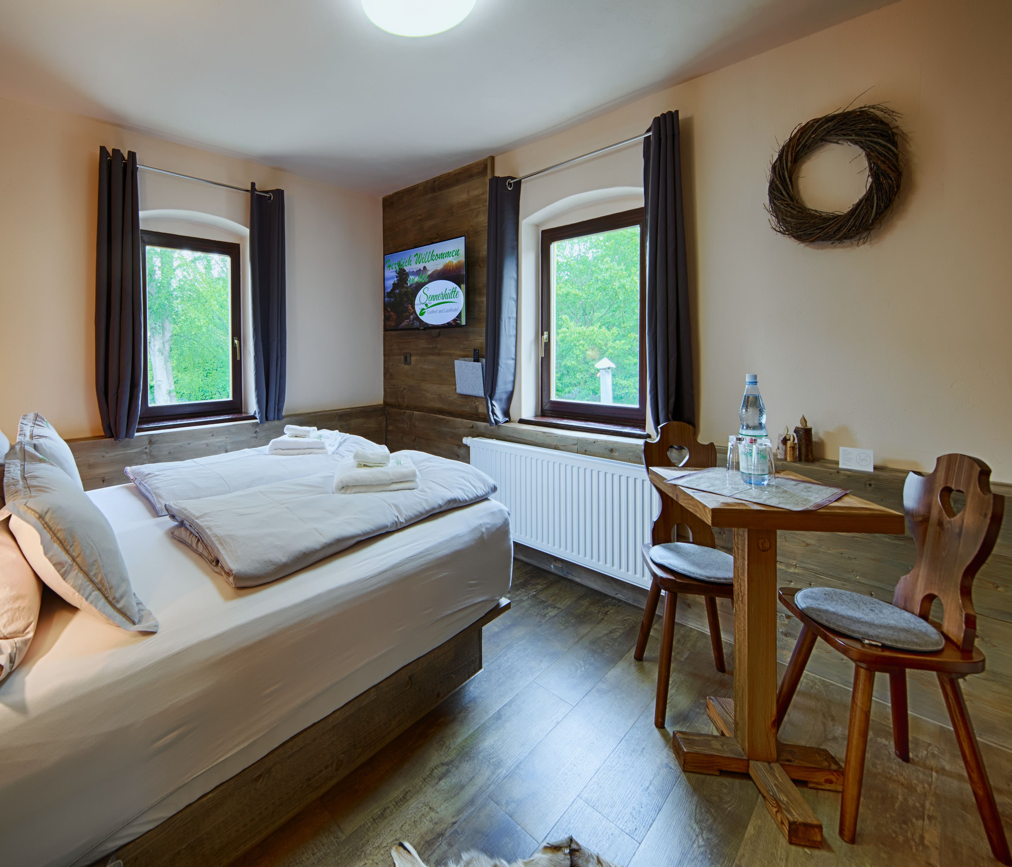 A hotel room with a bed, a table with chairs, a radiator, and a TV on the wall.