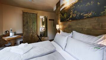 A hotel room with a large bed, a wooden headboard, a desk with a chair, a mirror, and a painting of a sunset on the wall.