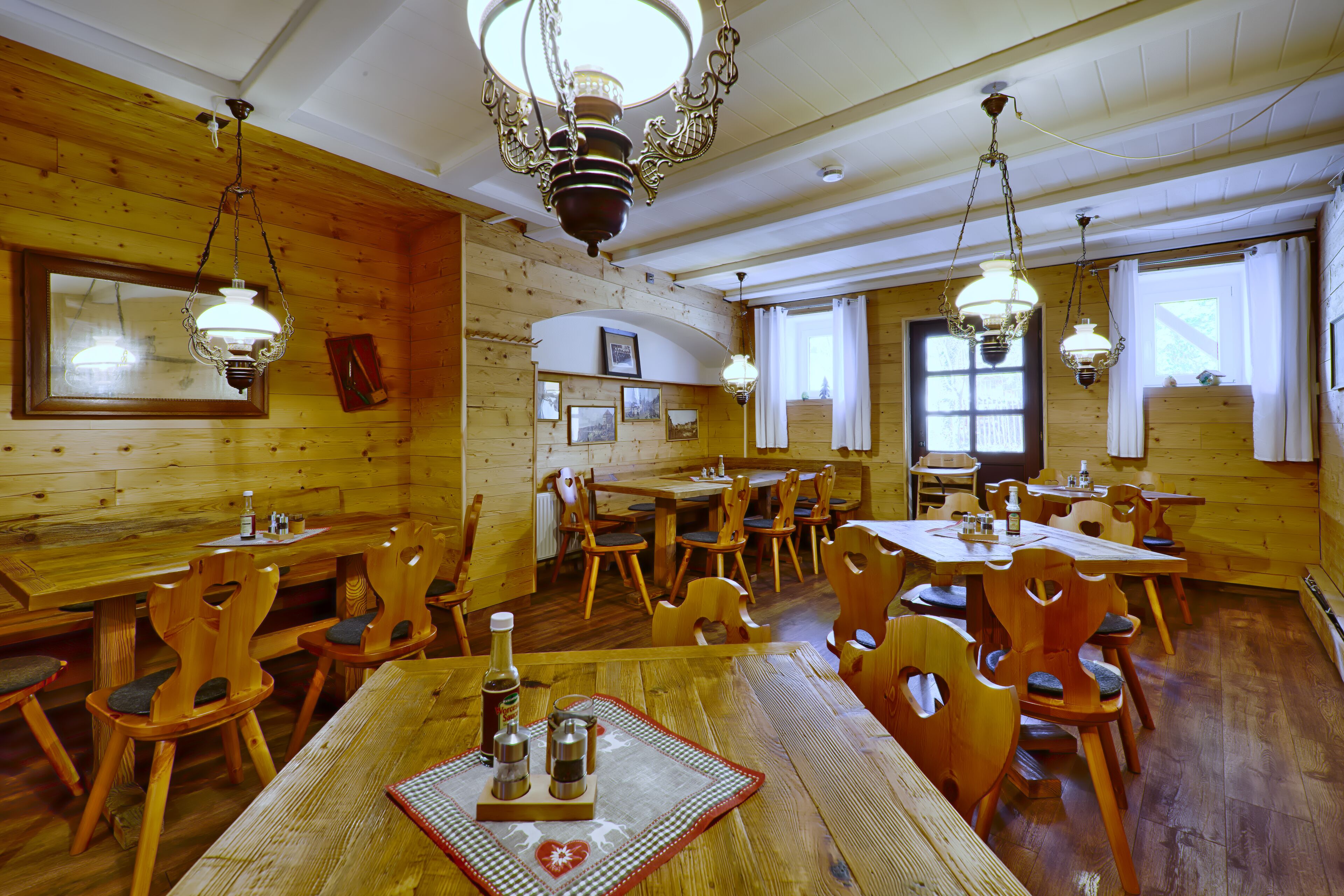 A wooden interior with multiple dining tables and chairs, chandeliers, and framed pictures on the walls.
