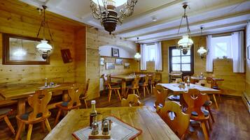 A wooden interior with multiple dining tables and chairs, chandeliers, and framed pictures on the walls.