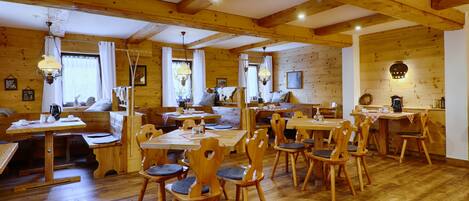 A wooden interior with multiple dining tables and chairs, wooden beams on the ceiling, and a rustic ambiance.