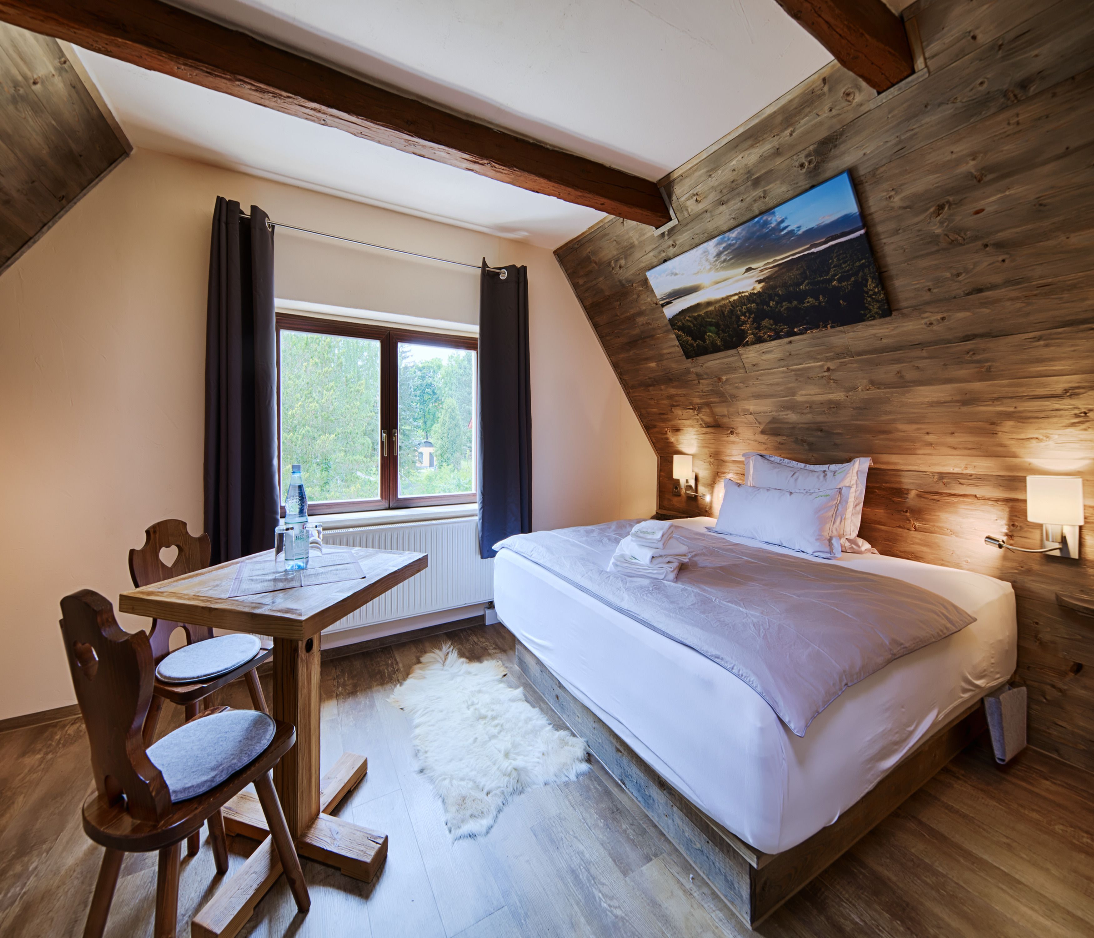 Une chambre avec un plafond en bois, un lit avec une literie blanche, un bureau avec une chaise et une fenêtre avec des rideaux.
