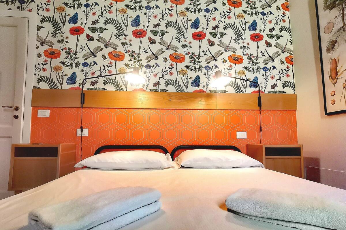 A hotel room with a bed, two bedside tables, and a floral wallpaper design.