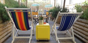Two beach chairs with striped cushions, a yellow cart with a potted plant, and outdoor tables and chairs in a courtyard. - Ostello Tasso (Florence)