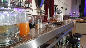 Uma área de bar com uma grande taça de ponche, um jarro de bebida de laranja e vários acompanhamentos.