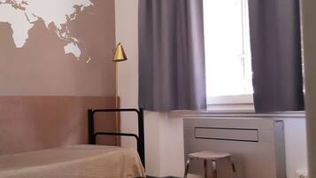 Une pièce comprenant un lit, un bureau, une chaise, un radiateur et une fenêtre avec des rideaux.