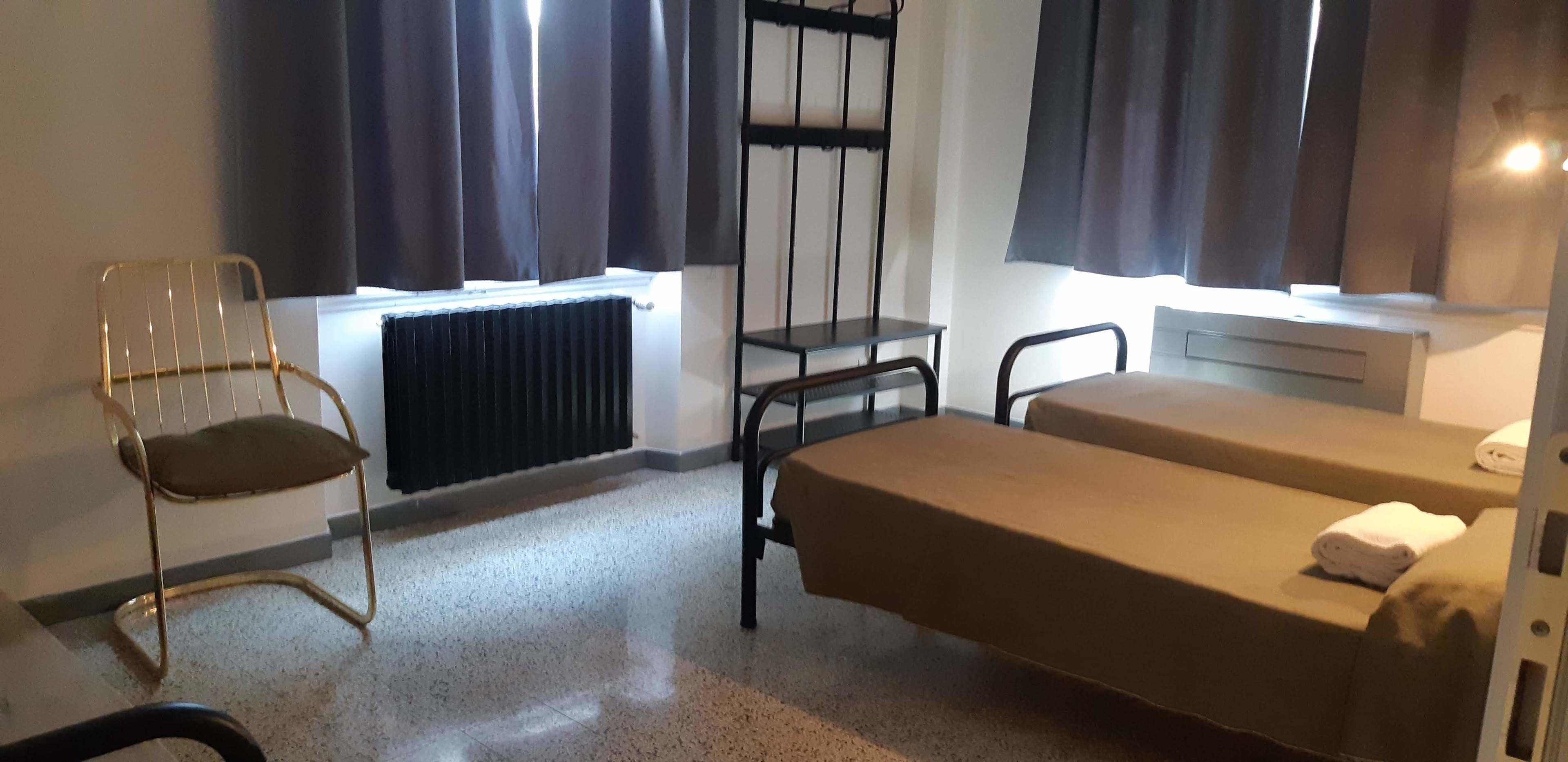 A small, simple room with a bed, a chair, a table, and a radiator.