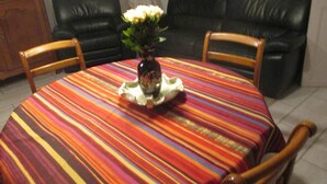 Een ronde eettafel met een kleurrijke streepjes tafelkleed, omringd door houten stoelen. Op de tafel staat een vaas met witte bloemen.