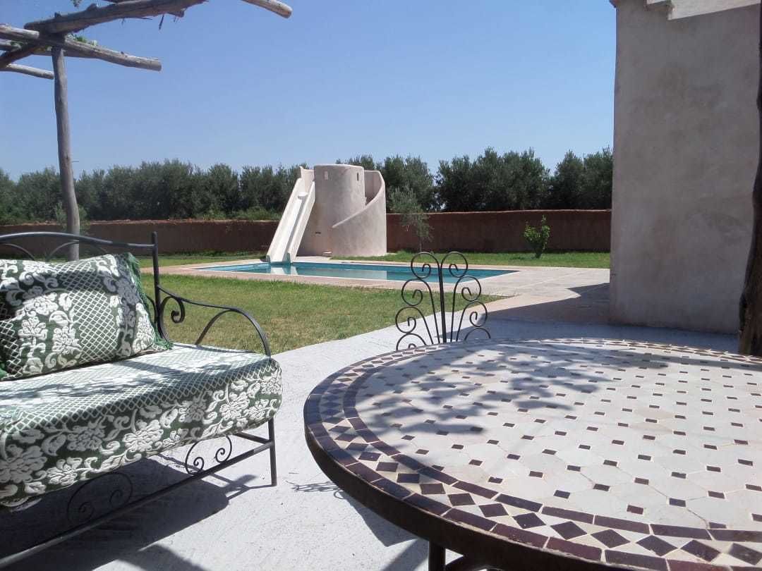 A patio area with a round mosaic table, a cushioned bench, and a slide leading to a pool.