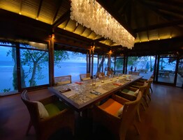 Un comedor con una mesa larga, sillas de mimbre y vista al mar.