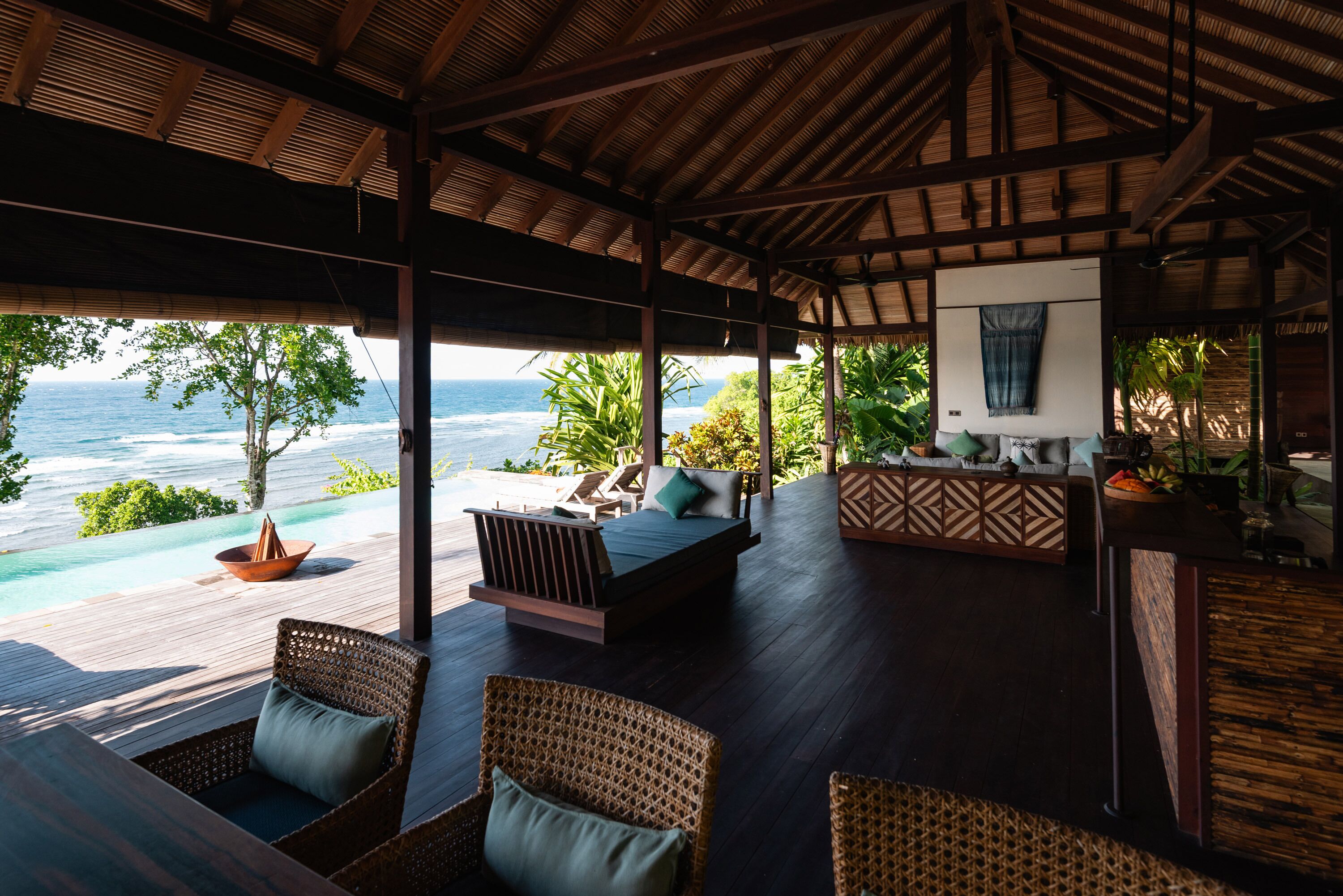 A covered outdoor seating area with a view of the ocean, wooden furniture, and a bar area.