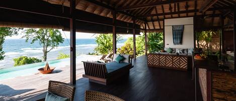 A covered outdoor seating area with a view of the ocean, wooden furniture, and a bar area.