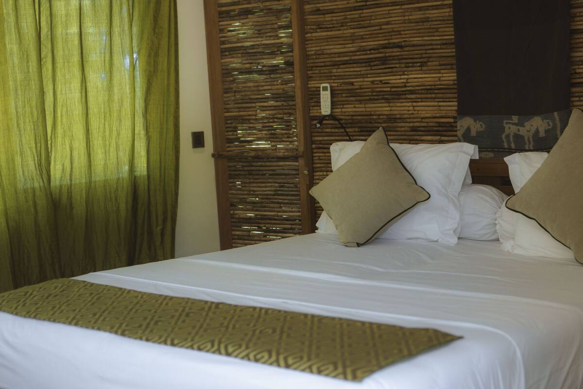 Quarto de hotel com cama, controle remoto na parede e manta decorativa.