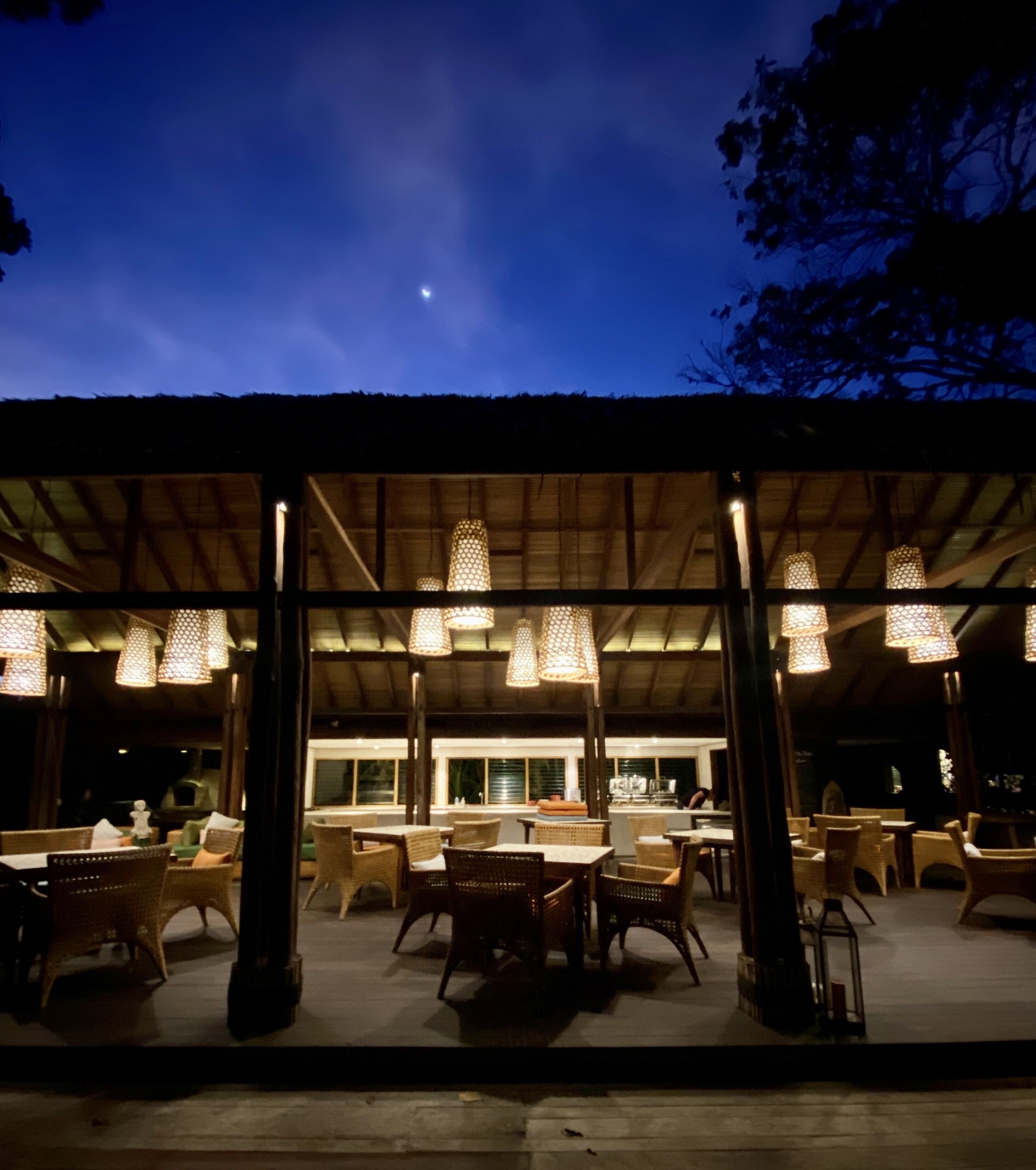 An outdoor dining area with wicker furniture and hanging lights, under a covered roof.