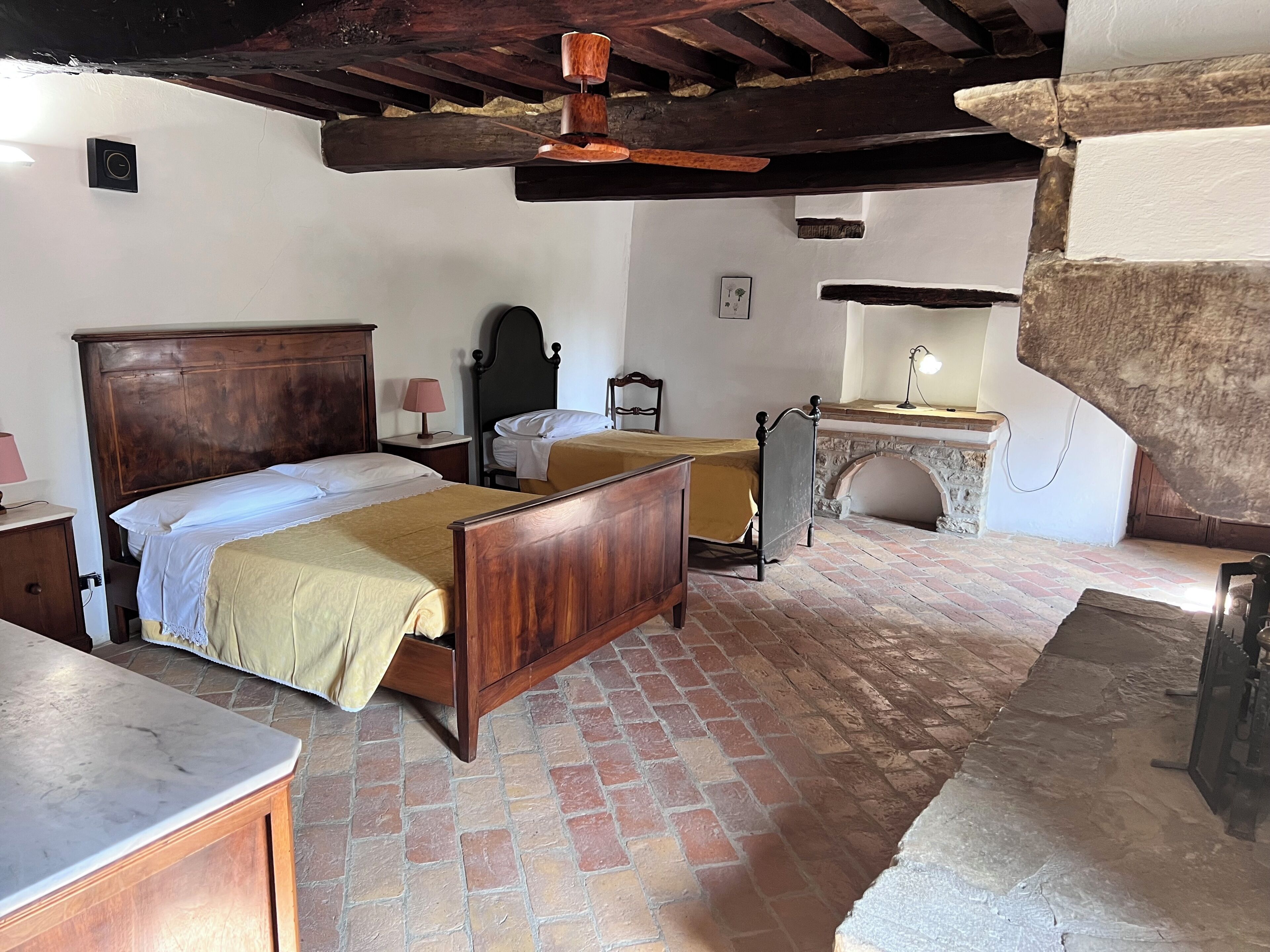 A traditional room with a wooden bed, a stone fireplace, and a tiled floor.