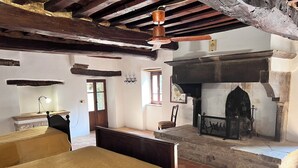 A rustic room with a fireplace, a bed with a headboard, a desk with a lamp, and a window.