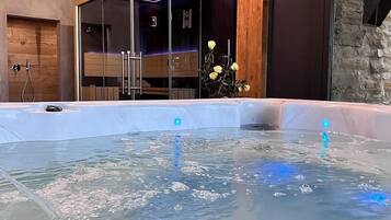 A hot tub with a wooden ceiling and stone walls, a glass enclosure, and a rose bush.