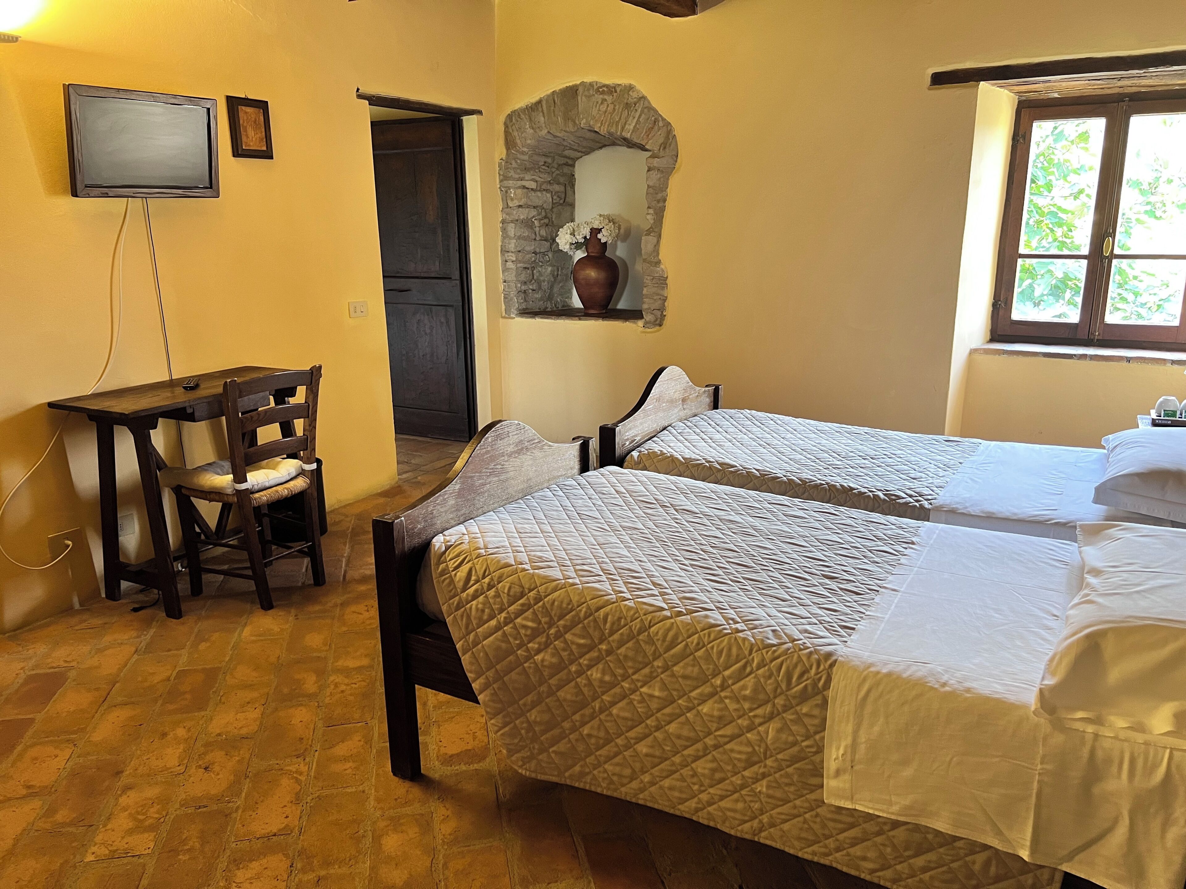 A room with two beds, a desk, a chair, a television, and a stone archway.