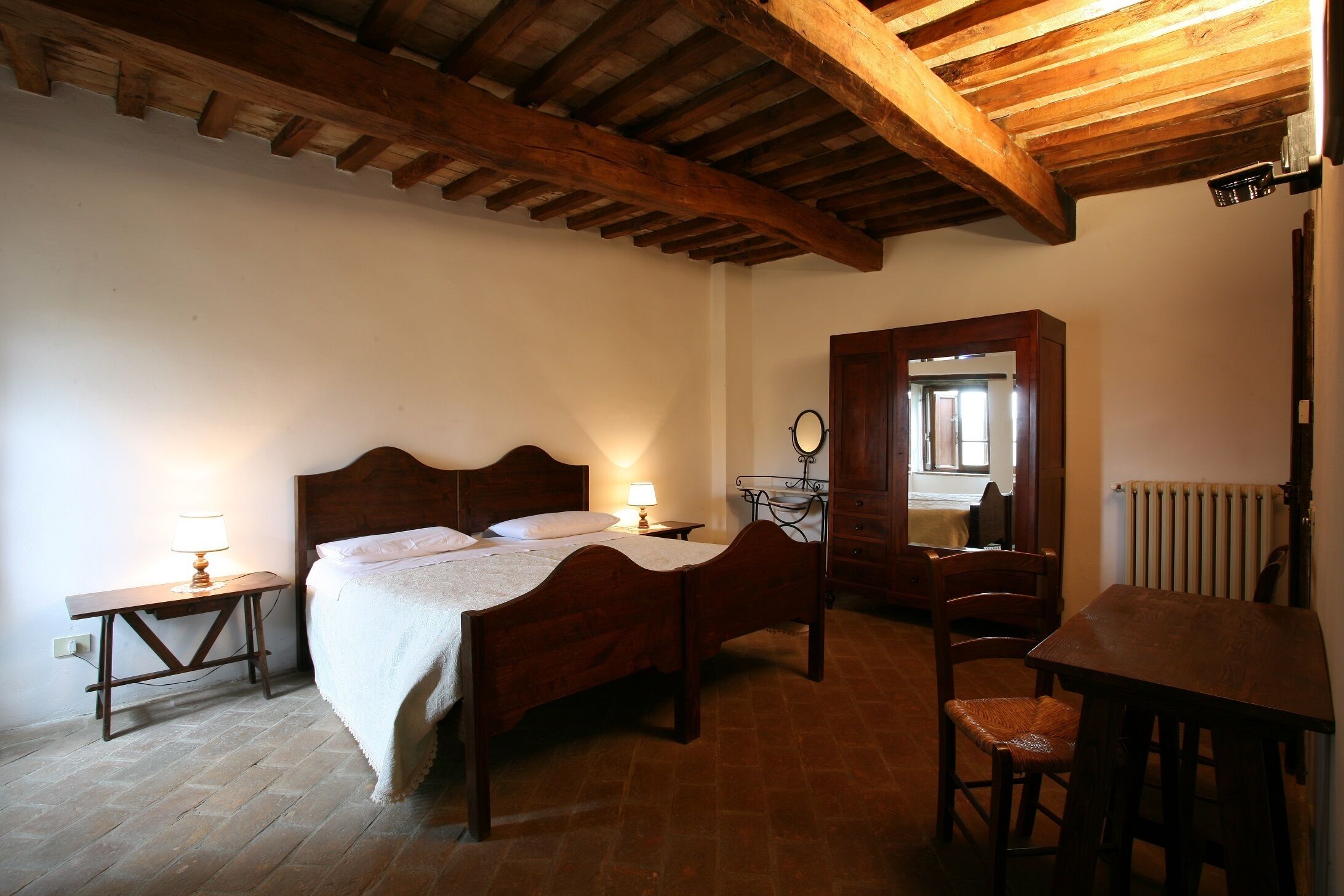 A bedroom with a wooden bed, bedside tables, a chair, a wooden desk, and a mirror.