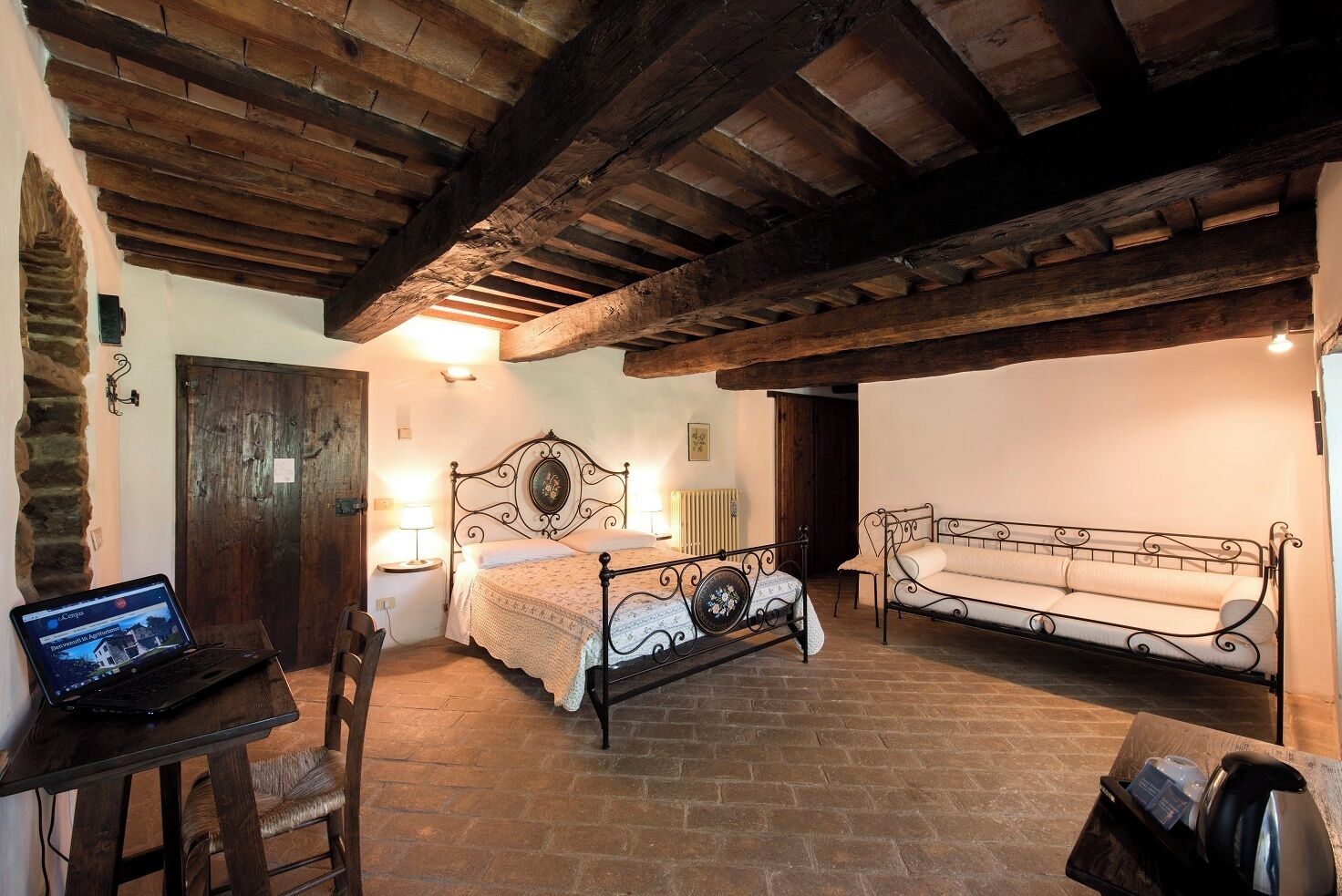 Une pièce rustique avec un lit, un canapé, un ordinateur portable posé sur une table et un mur en pierre.