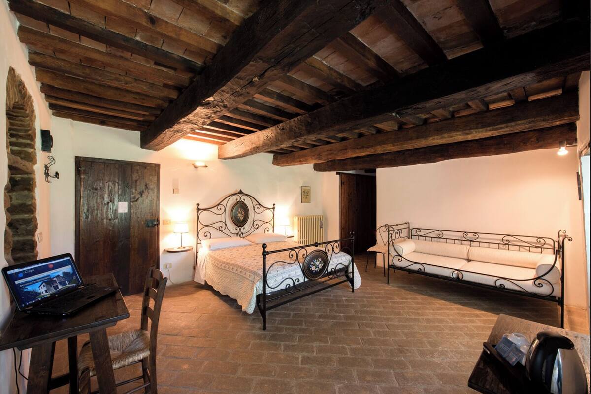 A rustic room with a bed, a sofa, a table with a laptop, and a stone wall.