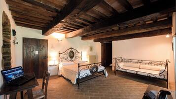 A rustic room with a bed, a sofa, a table with a laptop, and a stone wall.