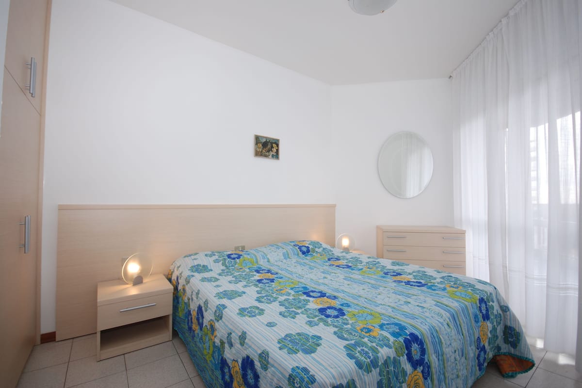 A bedroom with a bed, bedside tables, a dresser, a mirror, and a small picture on the wall.