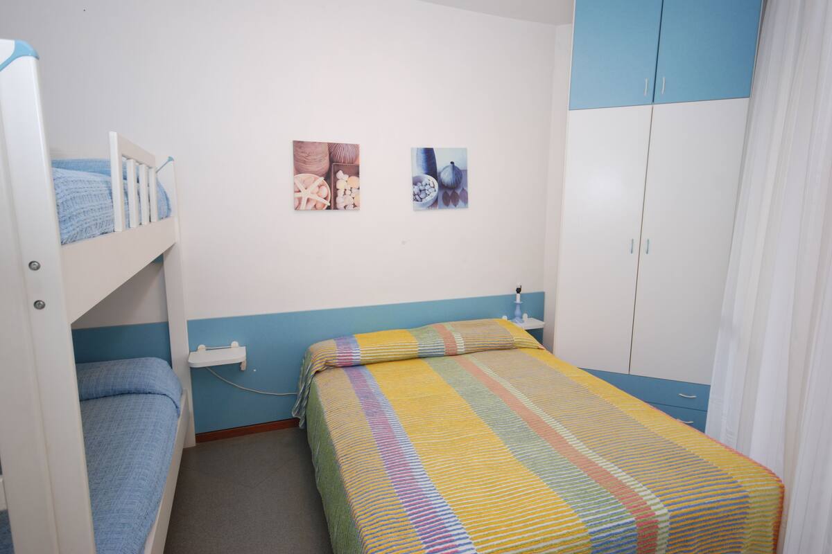 A bedroom with bunk beds, a bed with a colorful striped bedspread, a nightstand, and a wardrobe.