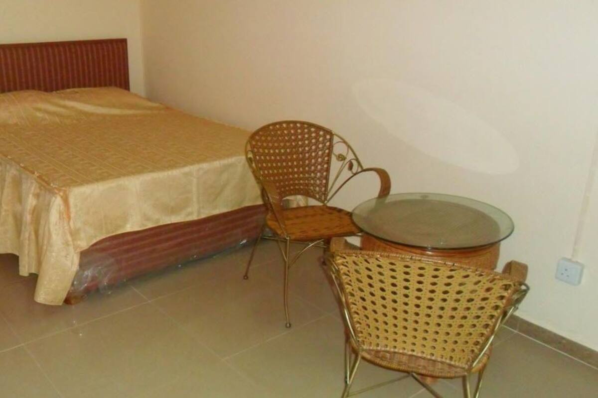 A bedroom with a bed, two wicker chairs, and a small round table.