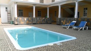 Una piscina con un muro de piedra y sillas reclinables azules.