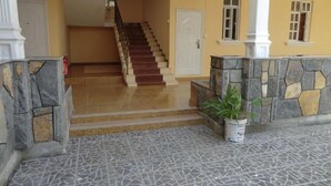 Una escalera que lleva a un piso superior, una pared de piedra con una planta en maceta y un suelo de baldosas.