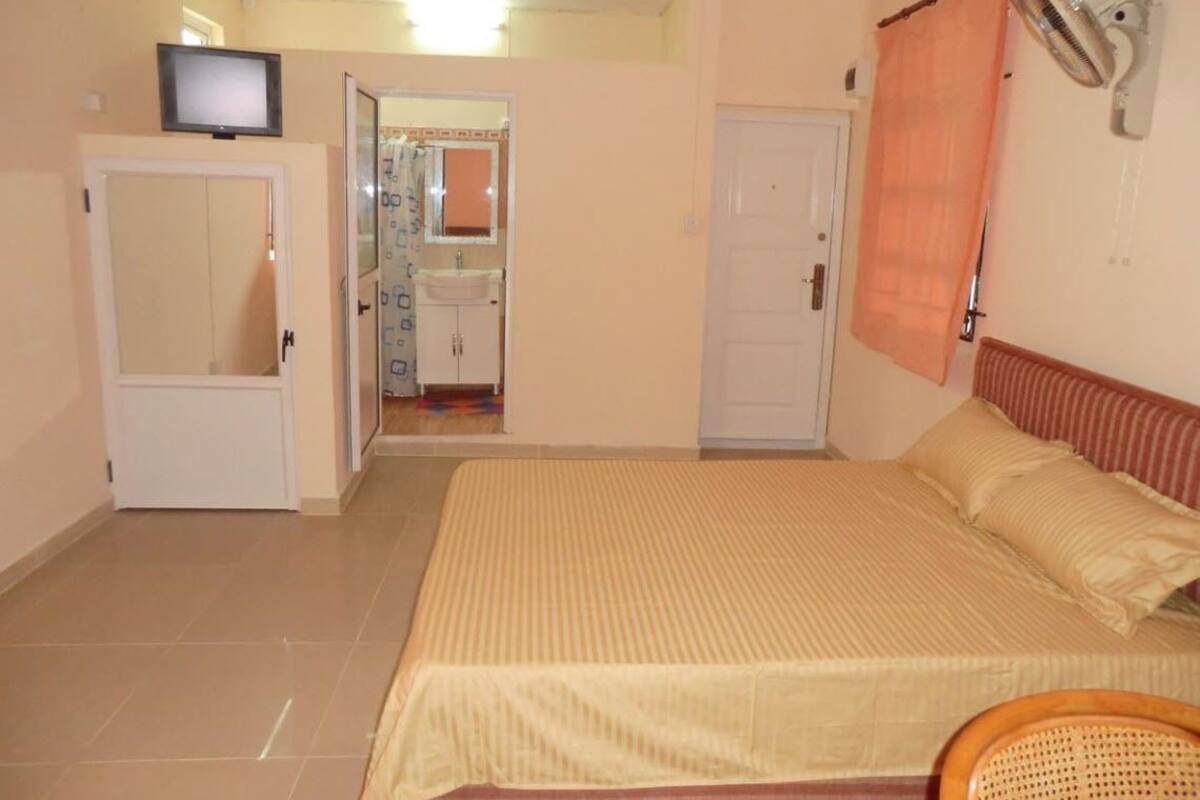 A bedroom with a bed, a television, a fan, and a bathroom visible through an open door.