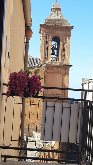 Un balcón con vistas a una torre campanario y un edificio con tejado de baldosas.