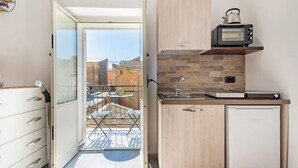 A compact kitchen with a microwave, a small refrigerator, and a sink. It features a sliding glass door leading to a balcony with a metal chair and a small table. - B&B Home Visit (Agrigento)