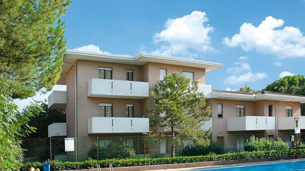 A multi-story residential building with balconies, a swimming pool, and a fenced garden area. - Residence Orsa Maggiore (Lignano Sabbiadoro)