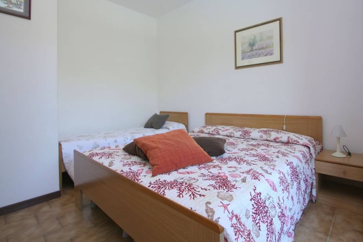 A bedroom with two beds, wooden headboards, a nightstand with a lamp, and a framed picture on the wall.