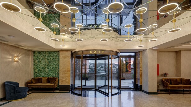 A modern lobby with a glass elevator, a circular exit door, and a green patterned wall. - Sole Palace (Tbilisi)
