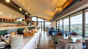 A restaurant with a buffet, seating area, and large windows offering a city view. - Sole Palace (Tbilisi)