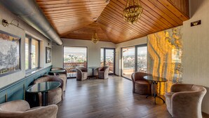 A spacious room with wooden flooring, a high ceiling, and large windows offering a city view. There are several seating areas with tables and chairs. - Sole Palace (Tbilisi)