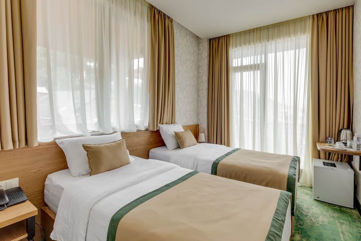 A hotel room with two beds, a desk with a telephone, a small refrigerator, and a TV mounted on the wall.
