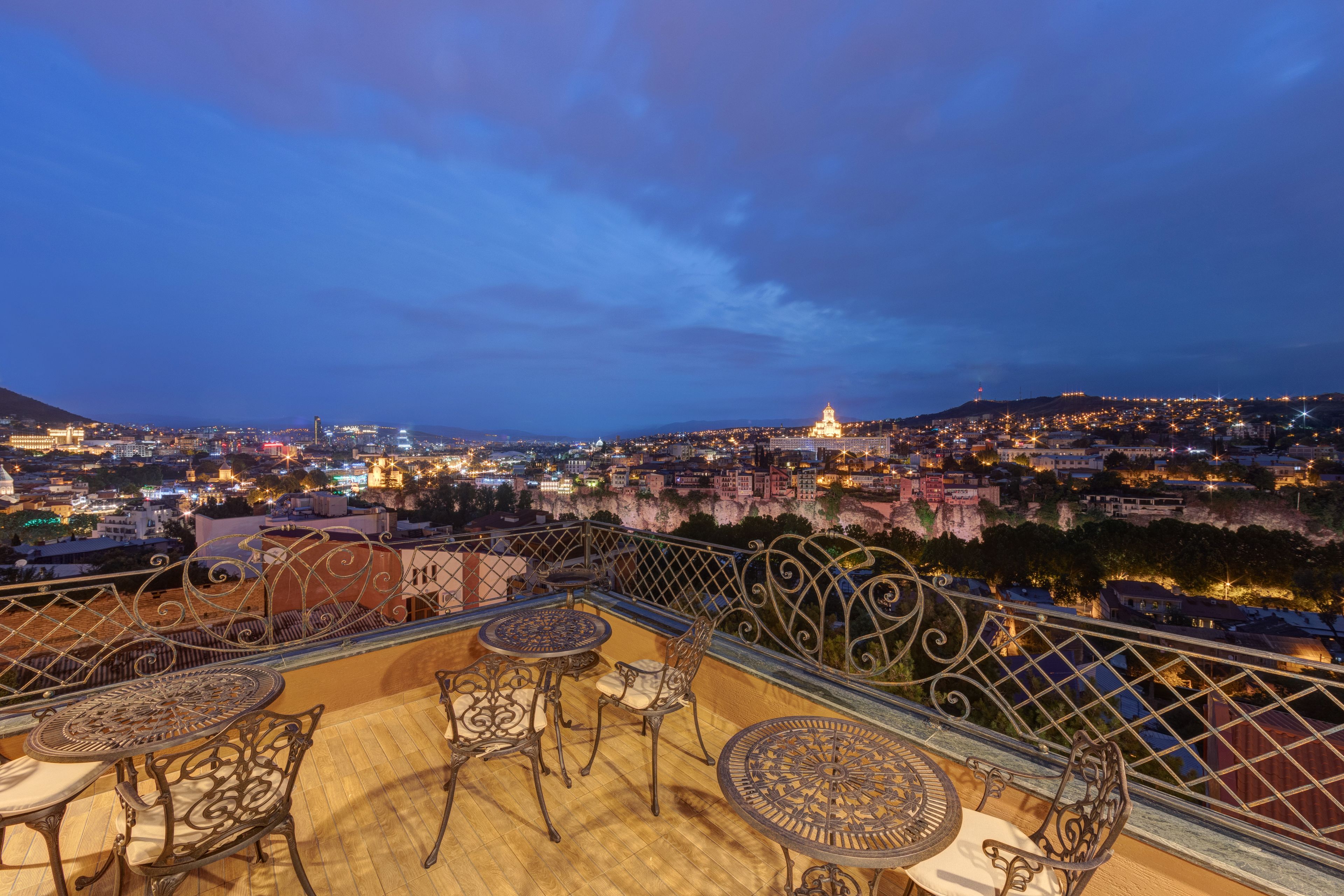 A rooftop terrace with outdoor seating and a panoramic city view at dusk.