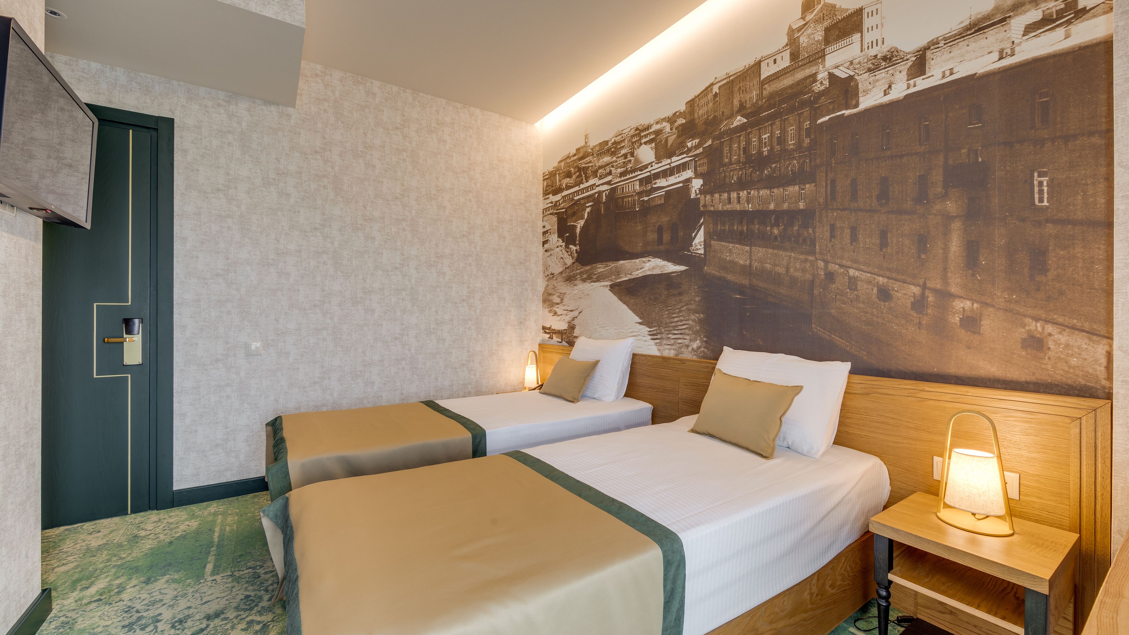 A hotel room with two beds, a nightstand with a lamp, a large wall mural, and a door with a keyhole.