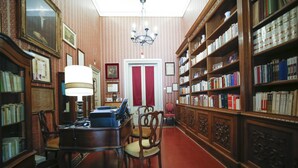 Una biblioteca con estanterías de madera, un escritorio con lámpara y una puerta con marco rojo.